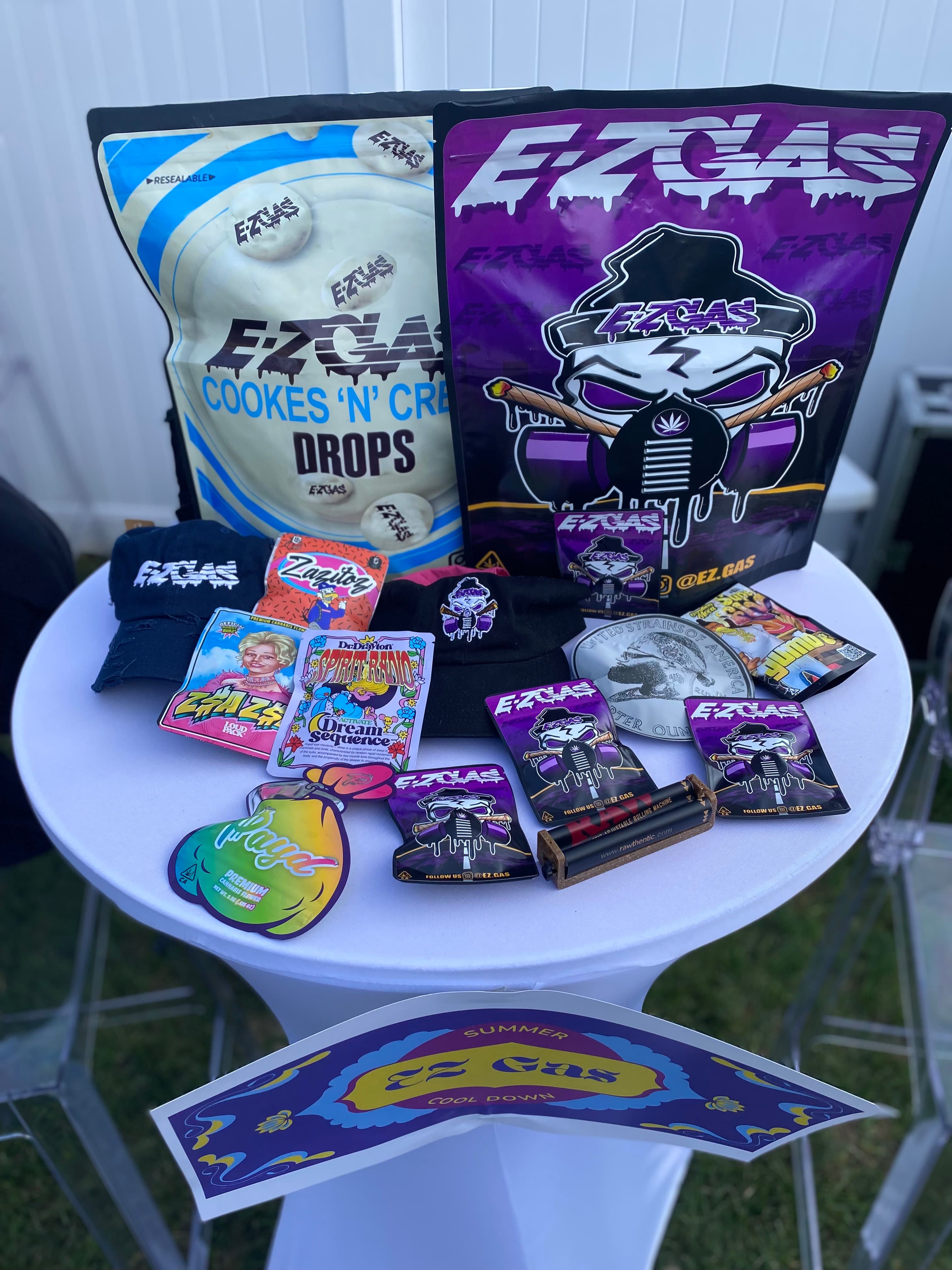Product spread on white table — bags, merch, stickers, event display